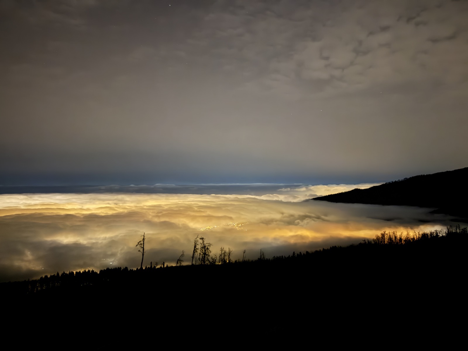 Byernes lys, der gløder gennem skyhavet om natten, set fra de skovklædte skråninger på vej op mod Teide
