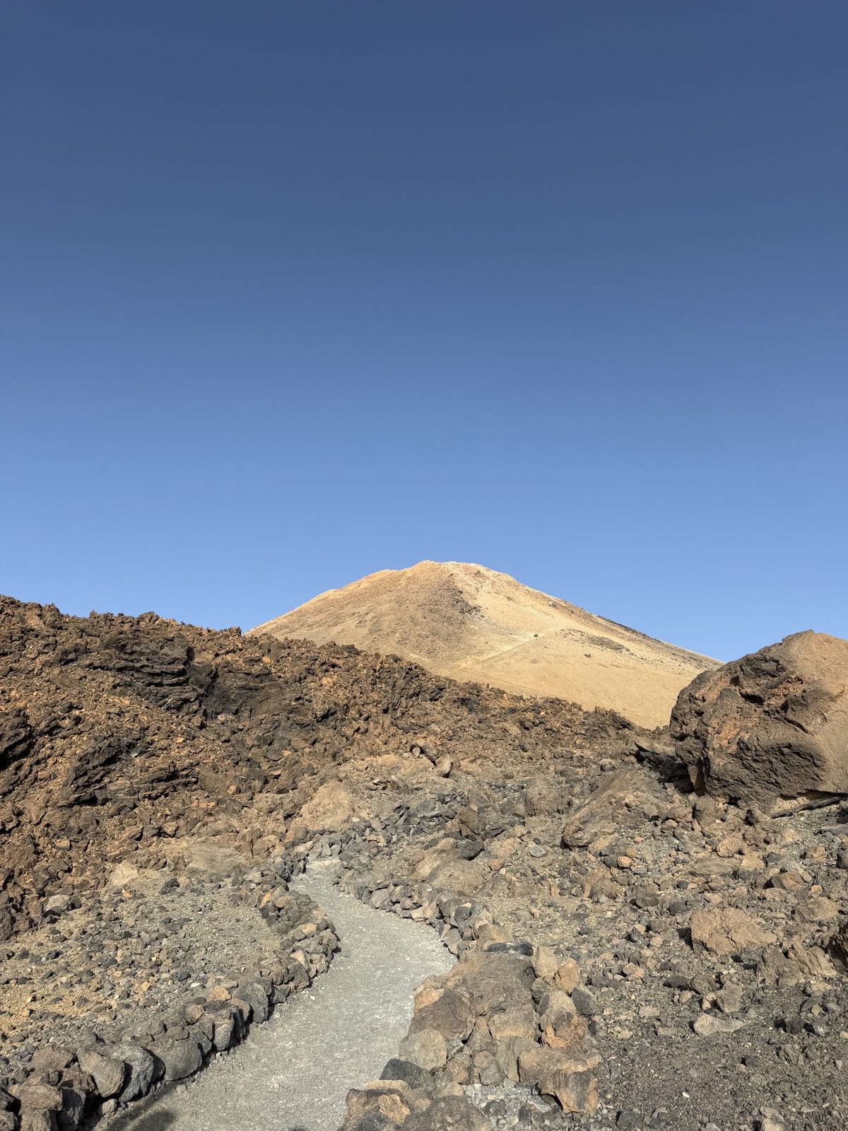 Stony path leading towards the bare summit cone of Mount Teide under a clear blue sky