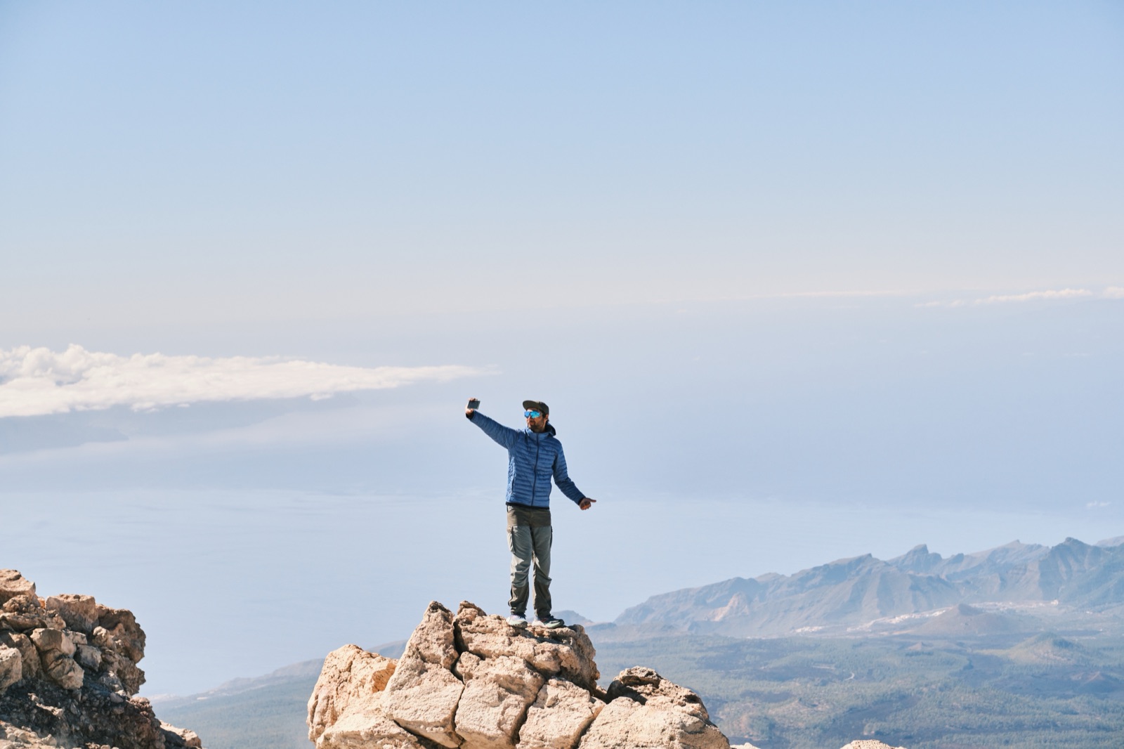 Hiker taking a photo from the summit rocks of Mount Teide, high above the coast and clouds