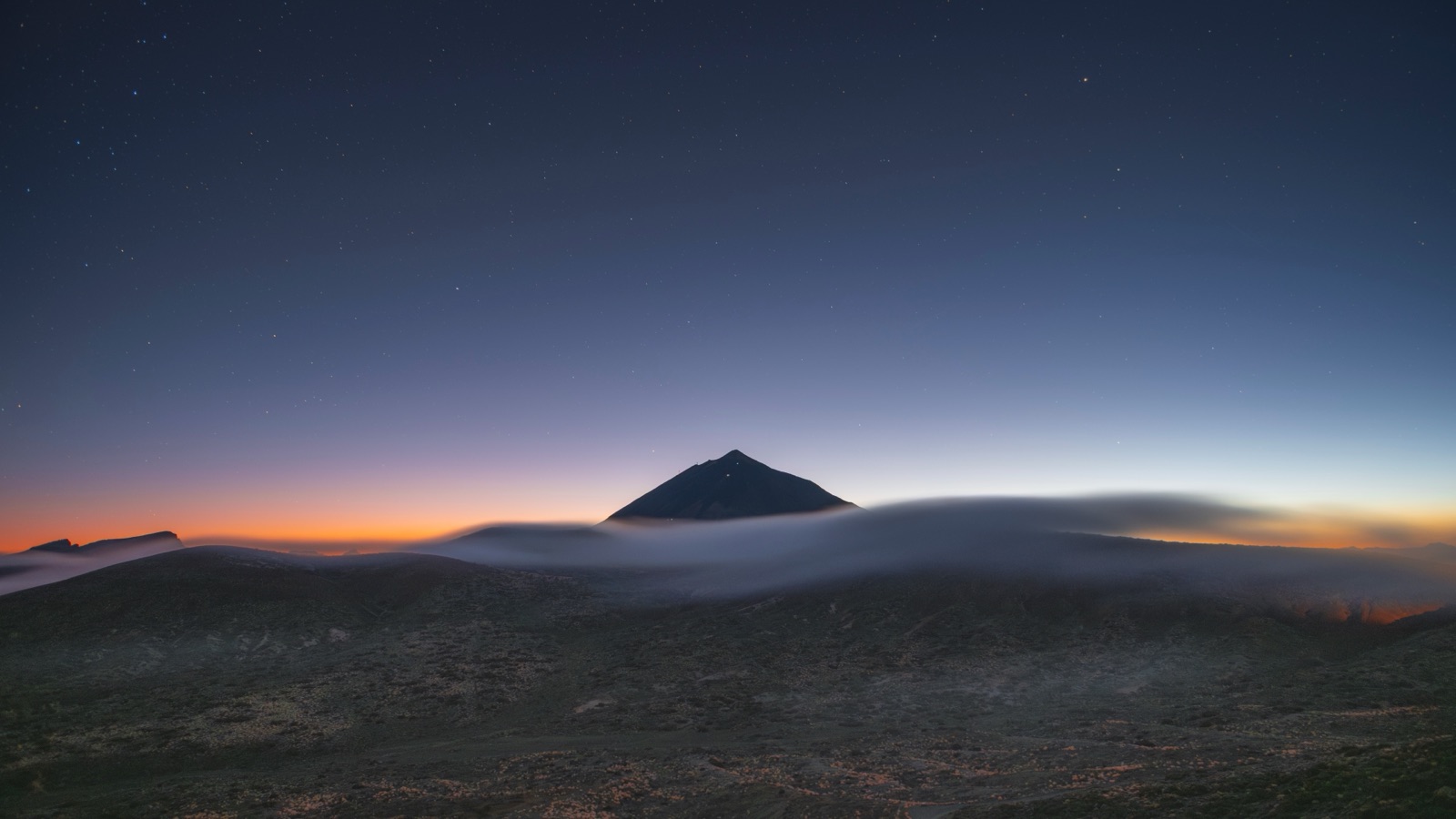Mount Teide silhouetted against an orange dusk horizon with the first stars overhead